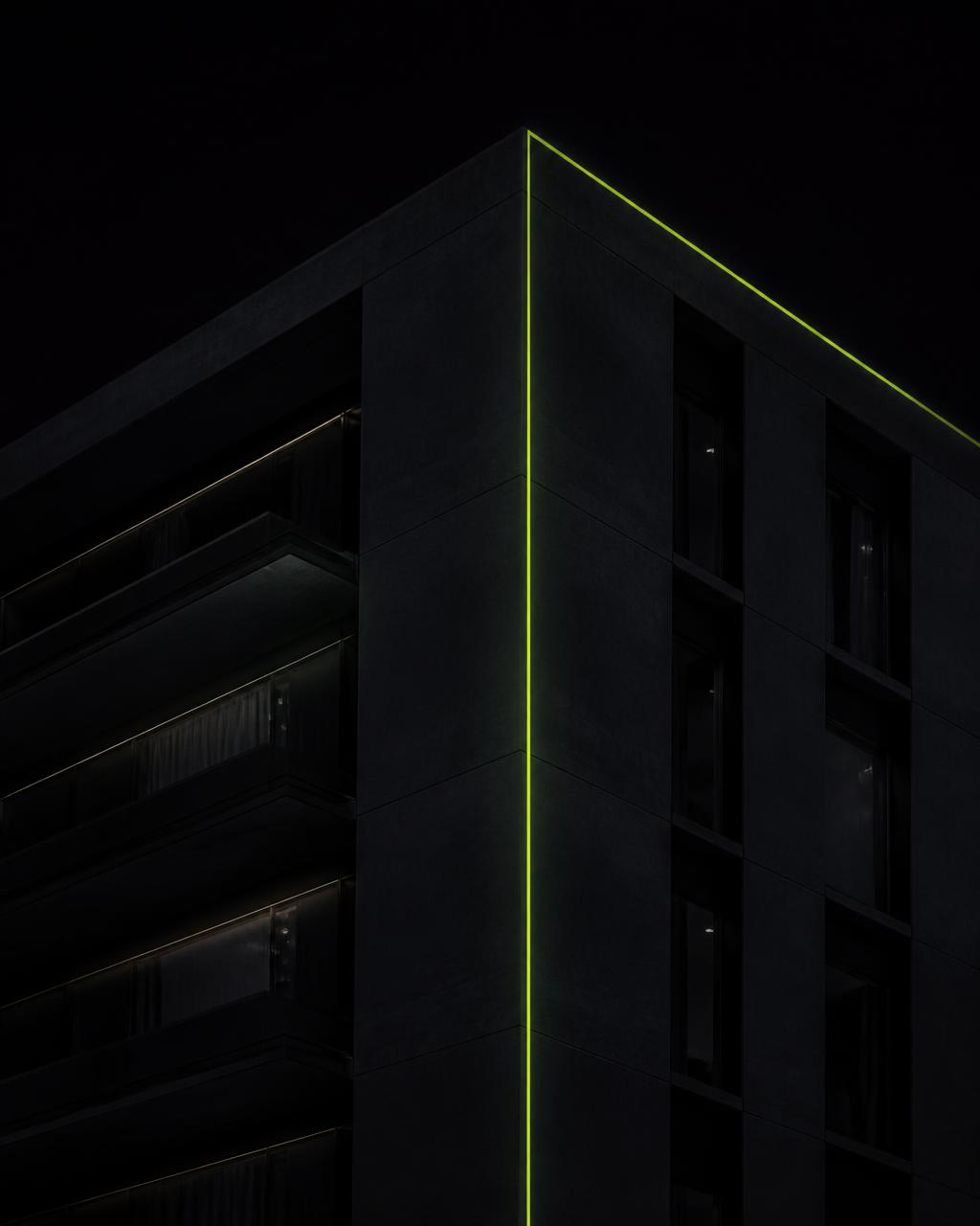 Fachada residencial em concreto e vidro à noite com uma linha de luz verde-limão na esquina